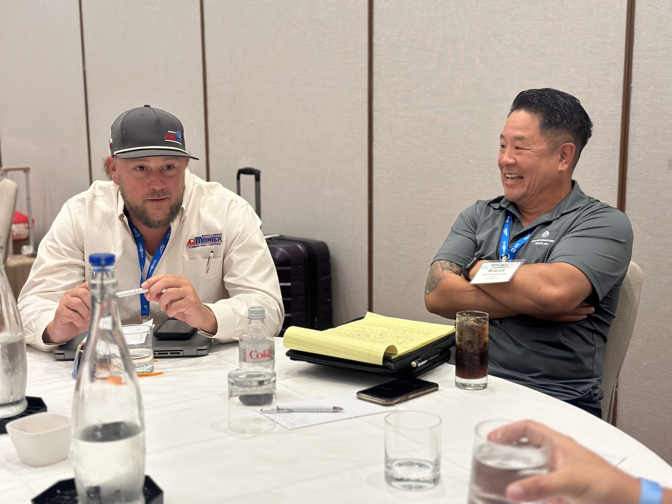 Peer Connection at Synergy Leadership Meeting Two HVAC professionals share ideas and laughter during a Synergy Solution Group peer group meeting focused on field leadership and collaboration.